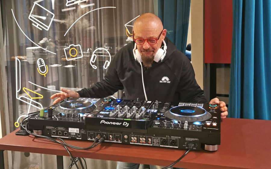 DJ Fredy za mix pultom, okružen rasplesanom publikom.